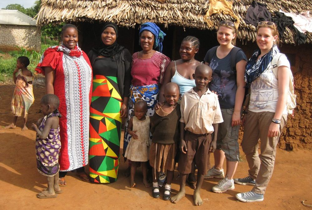 Patenkinder und Familien vor einer Hütte mit Besucherinnen aus Deutschland